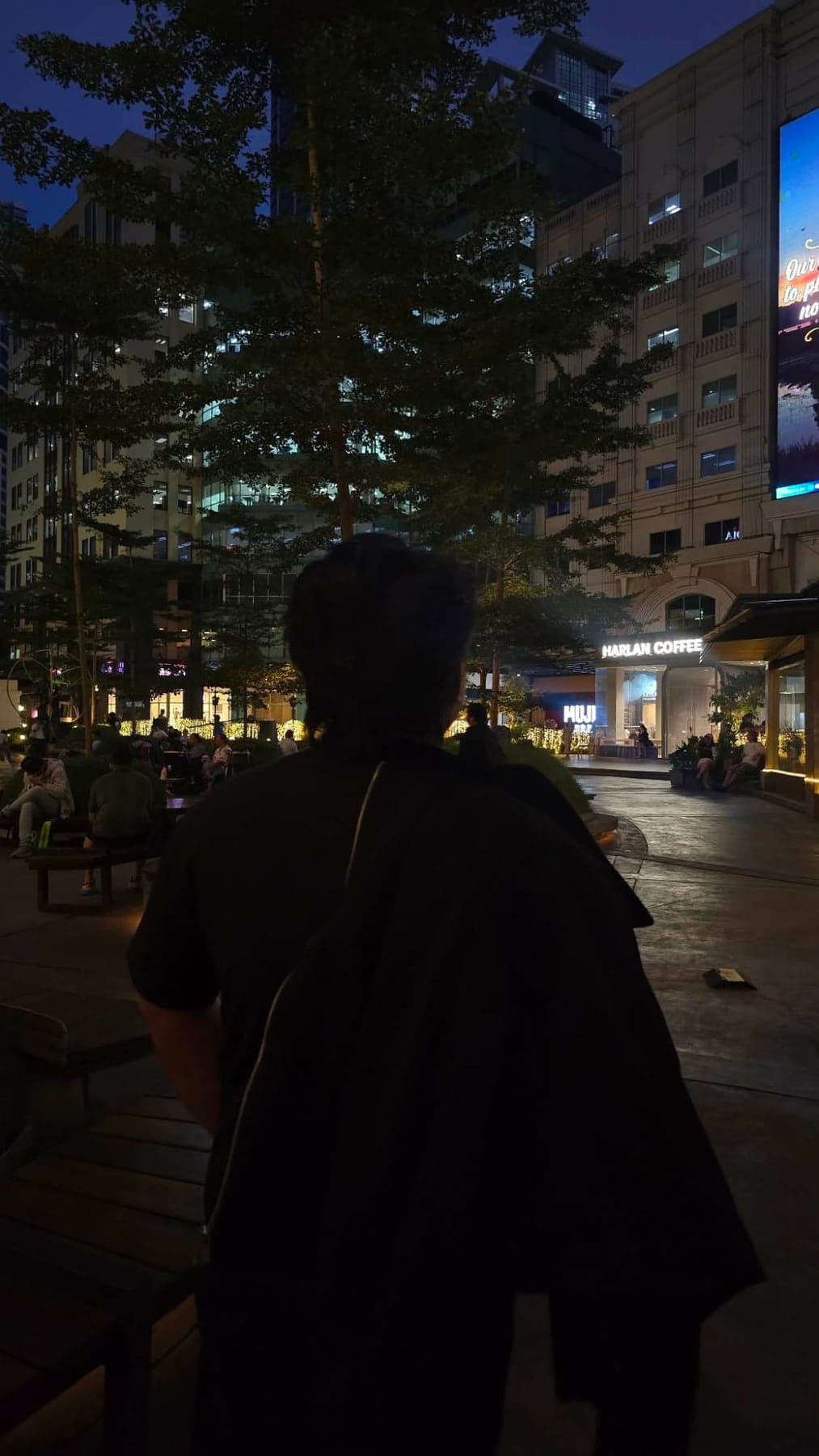 Me (Franz Eliezer Samilo), seen from behind in a black shirt, looking out over a lit city plaza at night